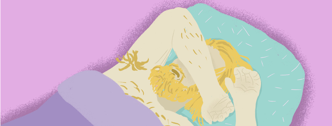 A blonde man with a beard is laying on a turquoise pillow under a purple blanket. He rests his arm on top of his face.