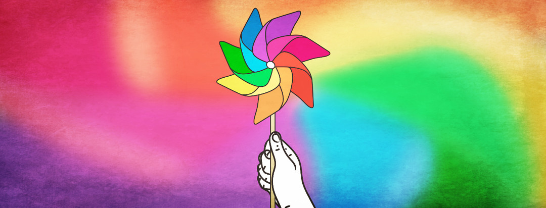 A hand holding a still pinwheel toy with a blurred mix of colors spinning in the background.