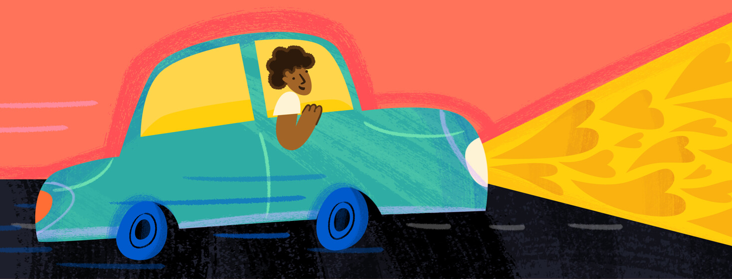 A smiling woman leaning happily out of a car passenger side window while headlights project hearts.