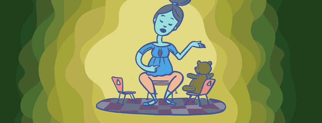 A woman is sitting facing 2 child size chairs. One chair has a teddy bear in it and she is practicing a speech while pointing at herself.