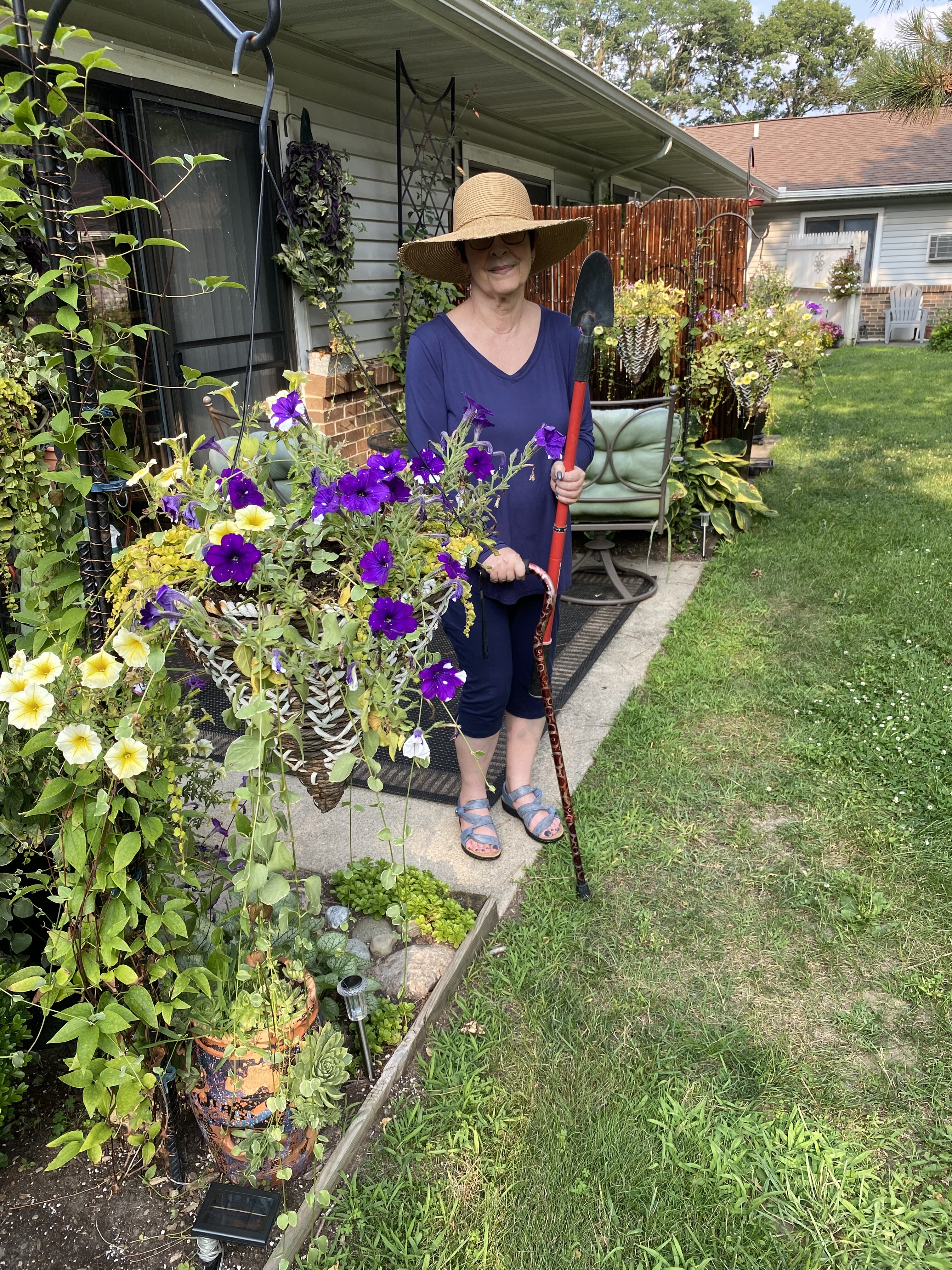 Kim in her gardening outfit, clutching a long handled trowel and cane.